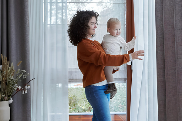 Vrouw met kind bij witte vitrage Vadain en grijze overgordijnen voor een tuindeur