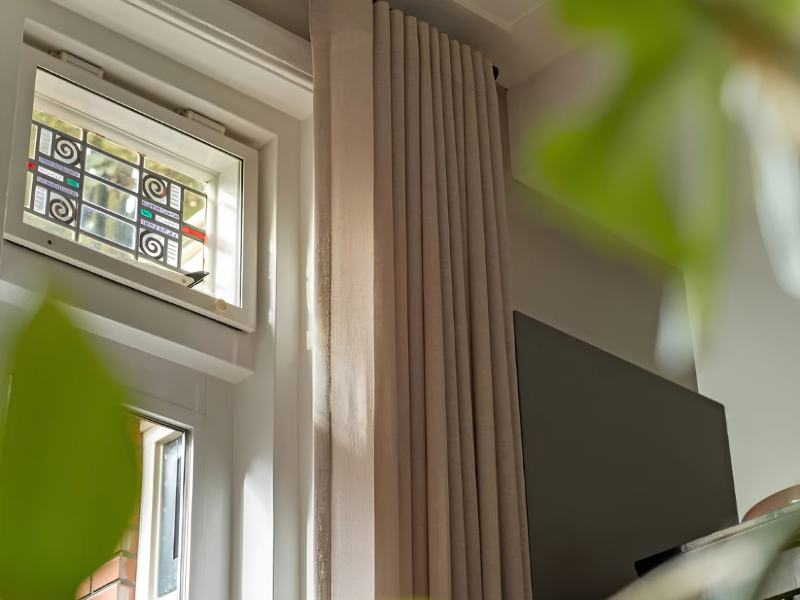 Hoge beige gordijnen bij glas-in-lood raam in warme woonkamer